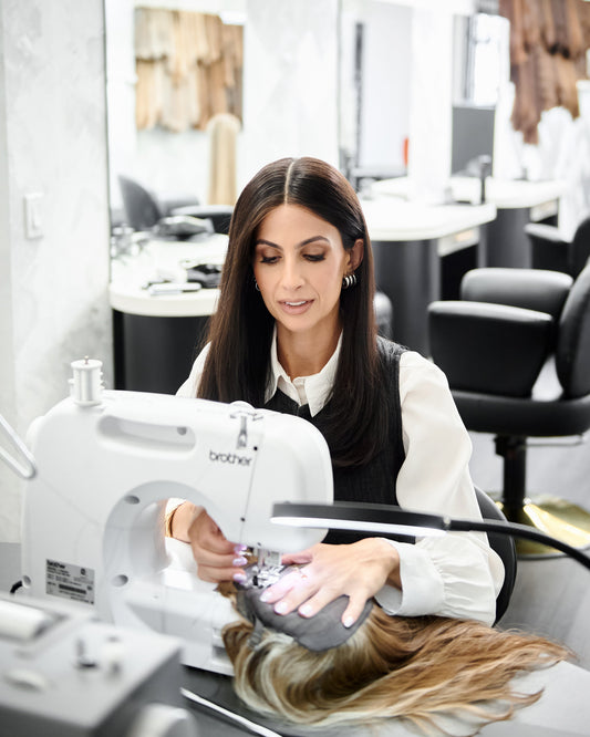 Tallie sewing human hair wefts at a machine in her Los Angeles wig workroom